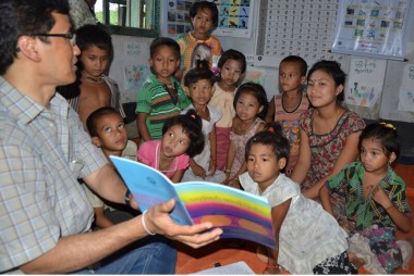 A man reads a story book to a group of small children in the Chittagong Hill Tracts, Bangladesh