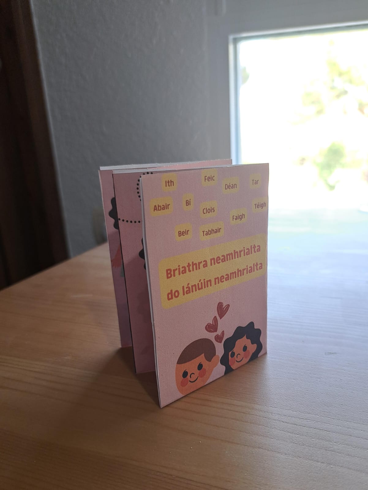 A pink zine with two people with hearts between them on the cover, folded and sitting on a table.