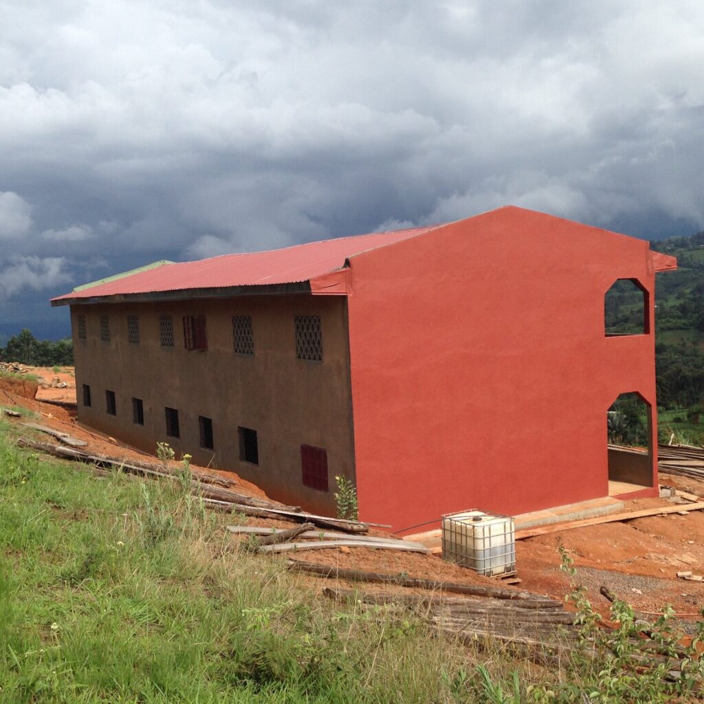 A newly constructed two-story school builting, painted bright red, sitting on a newly cleared plot of land in Babanki, Cameroon