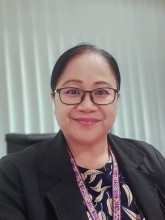 Dr. Jeannet Stephen, wearing glasses, a black jacket, and a colorful embroidered lanyard, smiling at the camera. 